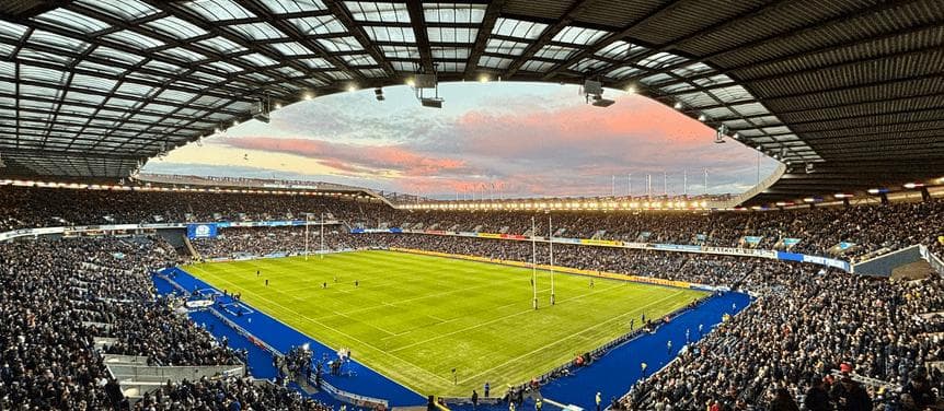 Modern football stadium interior at sunset with fans packed into all sides and the playing field visible from an elevated angle.
