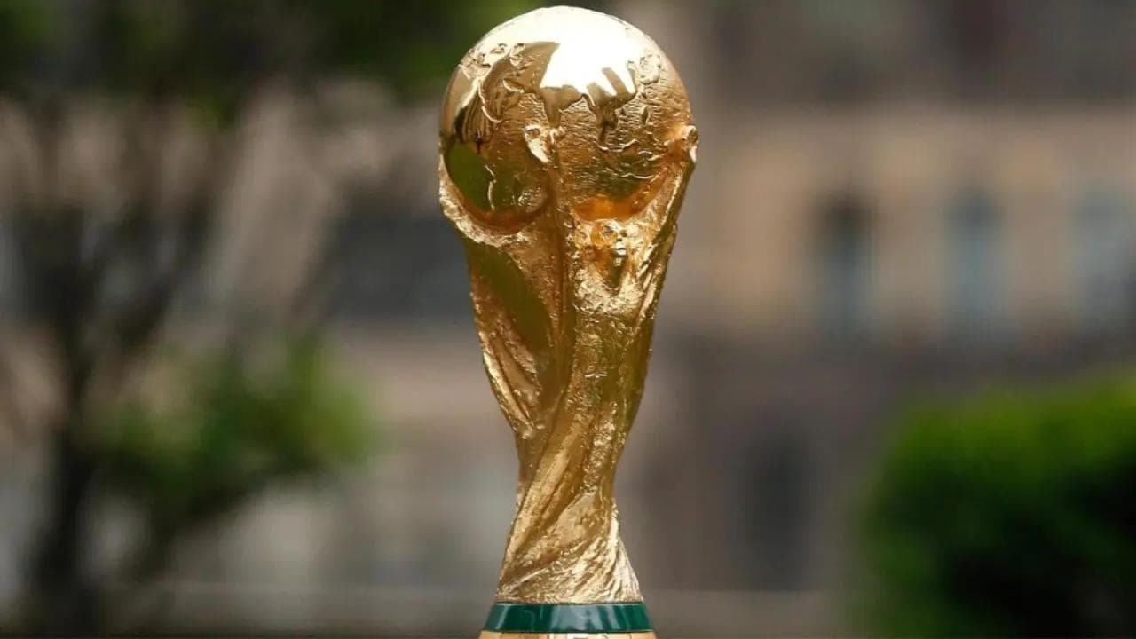 FIFA World Cup trophy displayed against a softly blurred green outdoor background, golden tournament prize ready for the 2026 edition.